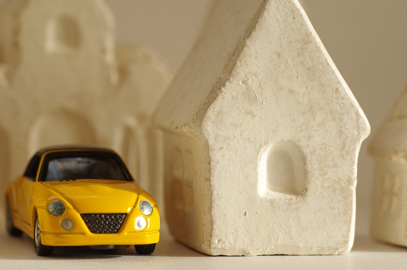 白い家の模型の横に停まる黄色い車のミニチュア